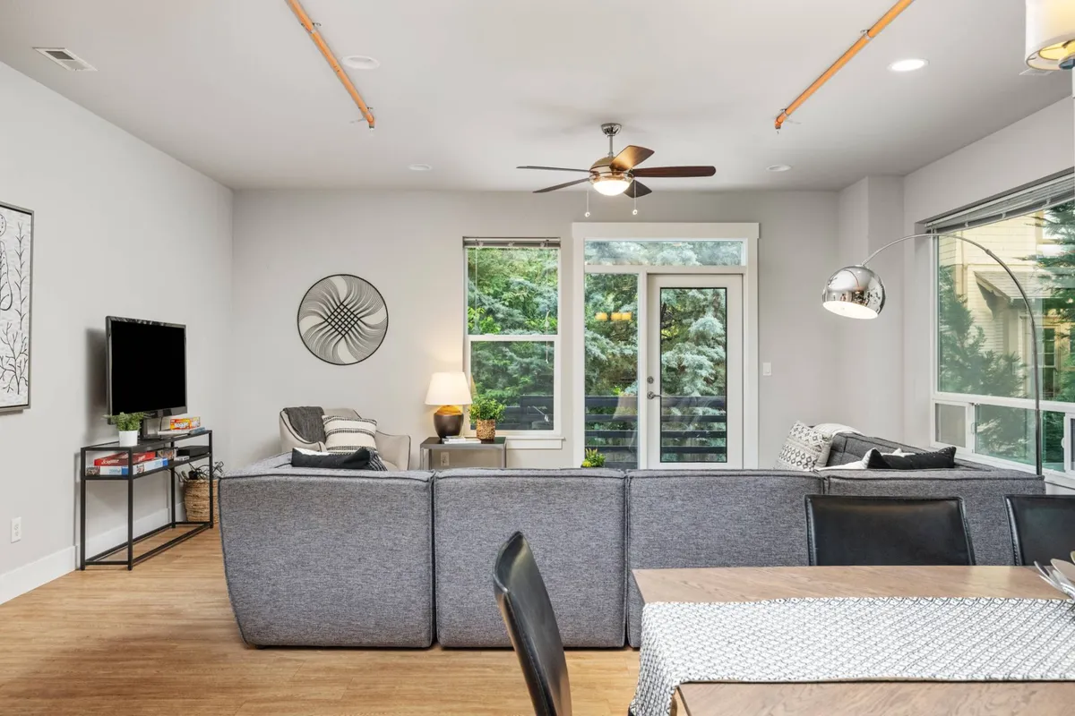 A cozy and stylish view of the living and dining areas, with a comfortable sofa, decorative wall art, ample windows, and a television. The setup encourages group activities, casual socializing, and enjoying natural light throughout the day.
