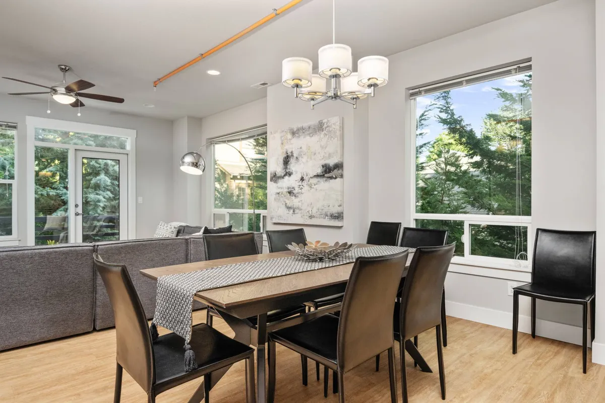 This image highlights a welcoming, contemporary interior with a dining table, prominent local artwork on the wall, large windows that fill the space with natural light, and a sofa nearby. The open layout and curated décor reflect the Pacific Northwest aesthetic described in the section.