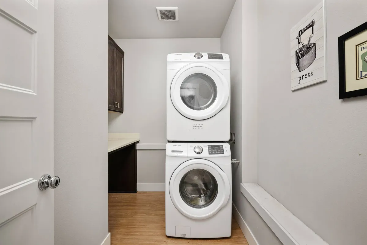 A laundry area with stacked washer and dryer, counter space, and practical cabinetry. The space is tidy and efficient, designed to support daily routines with ease.