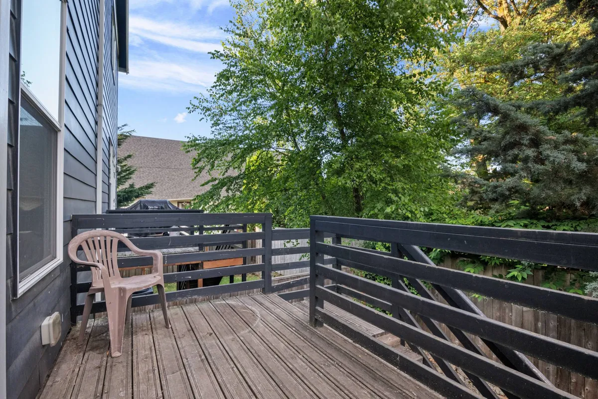 A serene wooden deck with a simple plastic chair set against a backdrop of tall green trees. The atmosphere feels peaceful, perfect for enjoying a quiet moment outdoors.