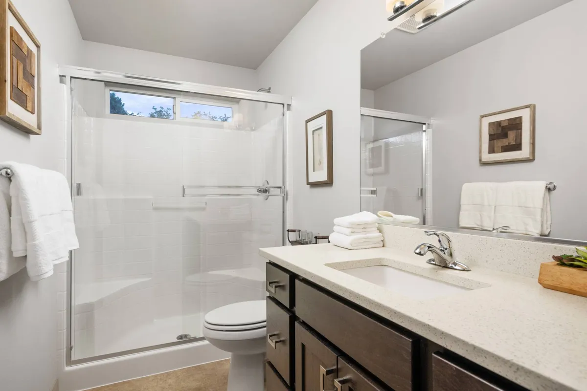 A calm bathroom scene with a modern shower, vanity with sink, and framed artwork. The space feels fresh and refreshing, ideal for personal grooming or a rejuvenating shower after a long day.