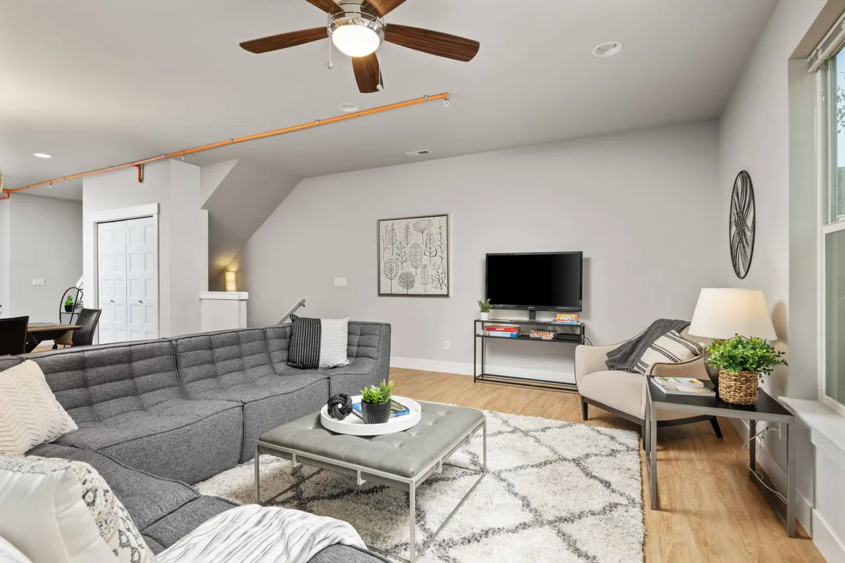 This image features a cozy gray sectional sofa, a coffee table, a TV stand, and eye-catching decorative wall art. The room’s lighting and arrangement provide a sense of warmth, togetherness, and modern style, echoing the tranquil and comfortable atmosphere of the entry and living spaces.